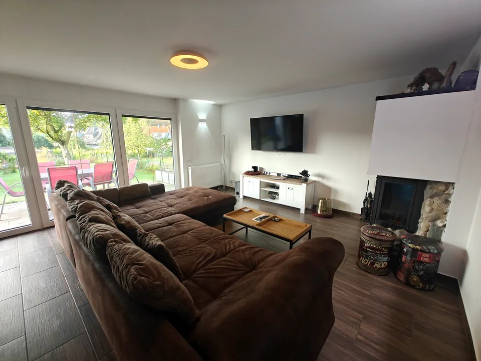 Living room with a large sofa, TV, wood-burning stove and windows onto the garden